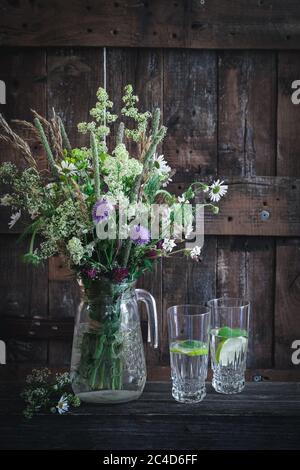 Paesaggio di campagna con fiori selvatici in vaso e bicchieri con acqua Foto Stock