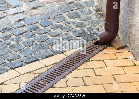 un sistema di tubi di drenaggio dell'acqua piovana sotto un marciapiede pedonale fatto di piastrelle in pietra e pavimentatrici con una griglia di ferro, primo piano. Foto Stock