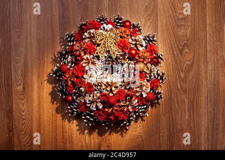 Corona di Natale di coni dipinti in rosso e bianco su sfondo ligneo di colore marrone. Foto Stock