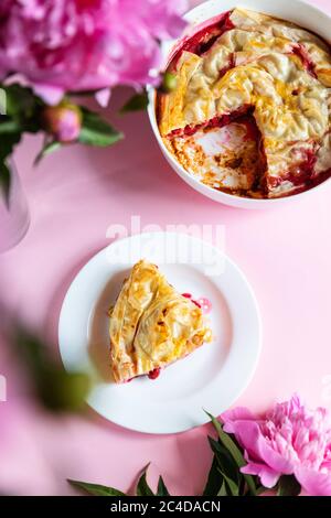 Vista dall'alto di un pezzo di torta di ciliegie con fiori di peonie su sfondo rosa Foto Stock