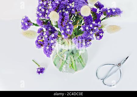 Vista dall'alto dei fiori blu selvatici in vaso di vetro su bianco con forbici da giardinaggio. Bouquet fai da te Foto Stock