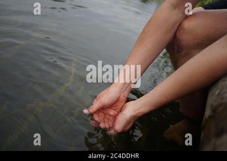 Mani che si tuffano in acqua di fiume Foto Stock