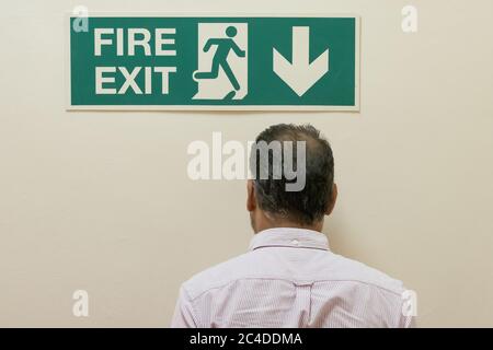 L'uomo ha visto camminare in un muro solido, sotto un cartello di uscita antincendio situato in un complesso di uffici. L'uscita effettiva del fuoco è sotto le scale. Foto Stock