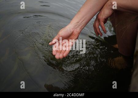 Mani che si tuffano in acqua di fiume Foto Stock