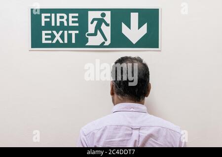 L'uomo ha visto camminare in un muro solido, sotto un cartello di uscita antincendio situato in un complesso di uffici. L'uscita effettiva del fuoco è sotto le scale. Foto Stock