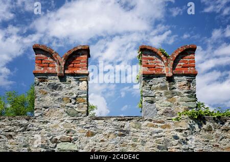 Mura di castello merloni su una parete fortificata in Italia con forma a coda di rondine e nuvole sullo sfondo Foto Stock