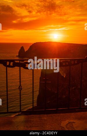 Un tramonto rosso ardente con la silhouette di una scogliera sul mare Foto Stock