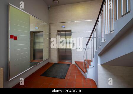 Interni con ingresso moderno nel complesso residenziale. Grande specchio, ascensore e scale. Tappeto su piastrelle rosse. Foto Stock