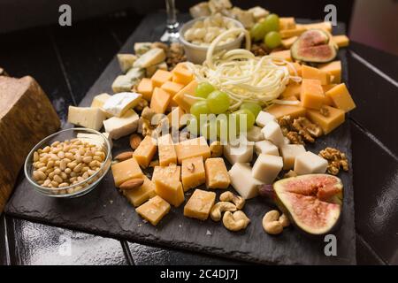 Cheeseboard o un assortimento di formaggi. Abbondanza di formaggi gourmet con fichi, uva e noci su tavola di legno nero. Ristorazione Foto Stock