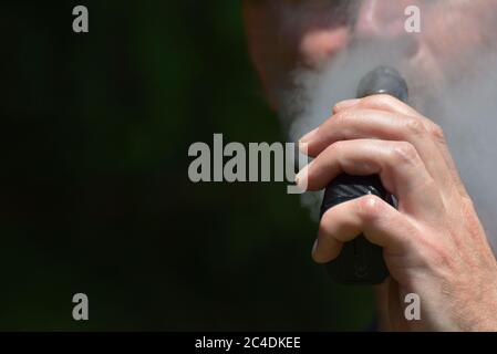 Un uomo che vaping con fuoco sulla sua mano come tiene la sigaretta / vape mod fino alla sua bocca mentre espala vapore Foto Stock