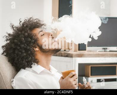 Vista del profilo di uomo shaggy fumo di e-sigaretta e bere caffè. Spazio di copia in nuvola di fumo bianca. Primo piano. Immagine colorata Foto Stock