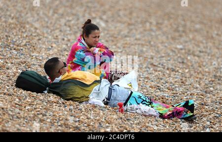 Una coppia si mantiene calda sulla spiaggia di Brighton mentre si prevede che temporali e pioggia torrenziale si infrangano in tutto il Regno Unito, portando alla fine una settimana di sole splendente e temperature brucianti. Foto Stock