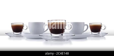 Una fila dinamica di bicchieri e tazzine bianche e di piattini pieni di caffè espresso liscio, su un bar o un tavolo bianco con fondo bianco Foto Stock