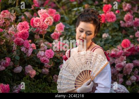 sposa donna in un antico abito storico vintage che si posa nel bellissimo giardino estivo di rose Foto Stock