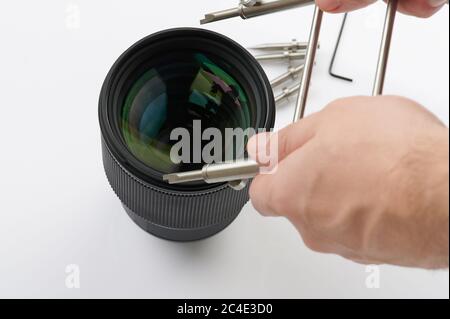 Servizio pulizia dispositivi ottici. Apertura di una lente moderna con un utensile Foto Stock