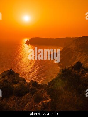 Un tramonto rosso ardente con la silhouette di una scogliera sul mare Foto Stock