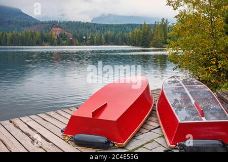 Lago di montagna Strbske Pleso con cime foggose sullo sfondo e barche rosse capovolte sul molo in primo piano. Focus sulle barche. Foto Stock