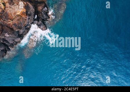 Vista aerea dall'alto delle onde turchesi dell'oceano Atlantico che si infrangono sulle rocce sulla riva portoghese dell'isola di Madera. Foto Stock