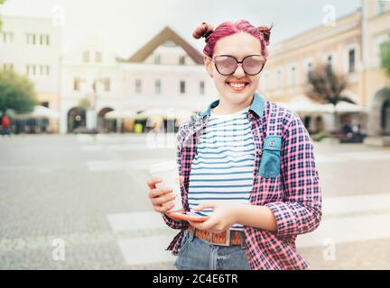 Ritratto di una bella giovane adolescente moderna con una straordinaria acconciatura in camicia a scacchi con berretto "caffè da andare" e smartphone sottile. Moder Foto Stock