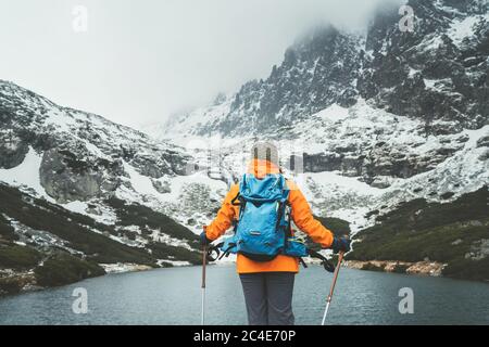 Giacca arancione vestito saccopelatore femminile con bastoni da trekking godendo la vista Velicke pleso (lago di montagna) durante la passeggiata in montagna in val Velicka Foto Stock