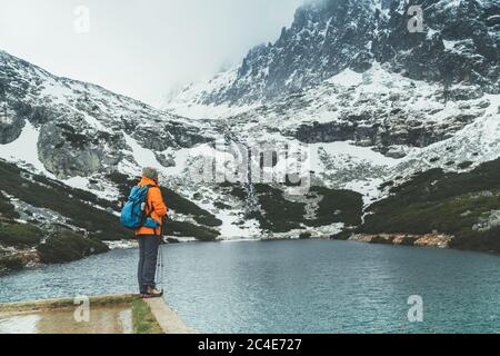 Vestito con giacca arancione brillante femmina zaino in spalla godendo la vista Velicke pleso (lago di montagna) come ha passeggiata in montagna nella valle di Velicka in High Tat Foto Stock