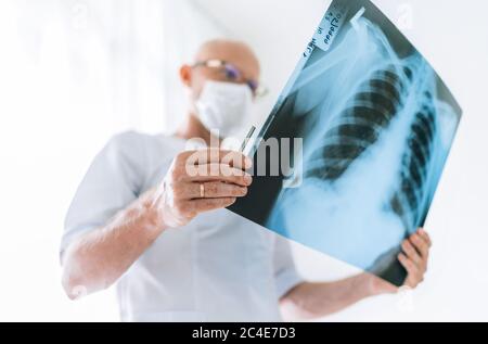 Medico maschile maturo che esamina il paziente radiografia polmonare pellicola del torace presso il reparto di radiologia in ospedale. Primo piano della scansione. Test radiografico del corpo di scansione Covid-19 Foto Stock