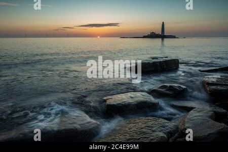 Guardando verso il faro di St Marys, Whitley Bay sulla costa nord-est dell'Inghilterra, Regno Unito. All'alba da una costa rocciosa. Foto Stock