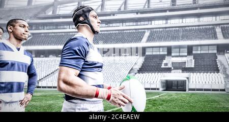 Immagine digitale composita di due giocatori di rugby che tengono la palla nello stadio sportivo Foto Stock