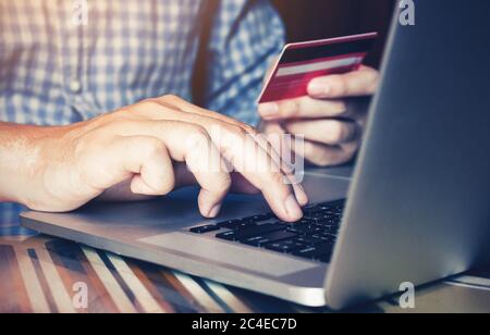 Mano dell'uomo che scrive sul laptop della tastiera e tiene la carta di debito per il concetto in linea di acquisto. Foto Stock