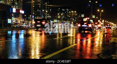 Notte piovosa in città. Strada bagnata, auto, riflessi di luci colorate e silhouette sfocate Foto Stock