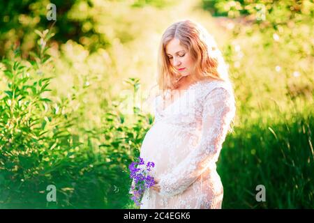 Bella giovane donna incinta rilassarsi nella natura in una bella giornata di sole con campo in background. Foto Stock