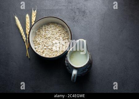 vista ad angolo alto di fiocchi d'avena non cotti e latte su sfondo nero Foto Stock