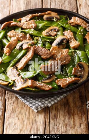 Manzo arrosto cinese con funghi e cialde di piselli verdi, semi di sesamo primo piano in un piatto sul tavolo. Verticale Foto Stock