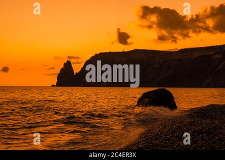 Un tramonto rosso ardente con la silhouette di una scogliera sul mare Foto Stock