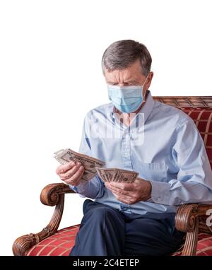Uomo caucasico senior che conta alcune bollette in dollari USA. Indossa una maschera facciale per prevenire il coronavirus. Isolato su sfondo bianco Foto Stock