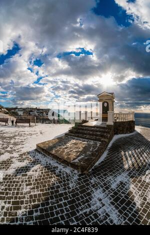 Vista panoramica grandangolare sul parco innevato sul terrapieno sullo sfondo del mare blu d'inverno. Passeggiata con una splendida vista sul Foto Stock