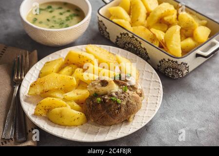 Gambo di vitello brasato servito con patate al forno e salsa di cipolla. Foto Stock
