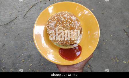 Primo piano di un hamburger con stagame sopra rabboccare e ketchup in un piatto giallo Foto Stock