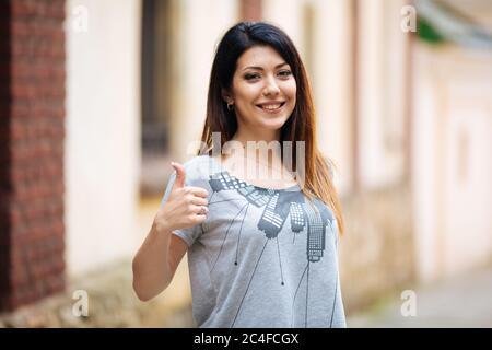 ragazza che mostra i pollici, sorridendo in città Foto Stock