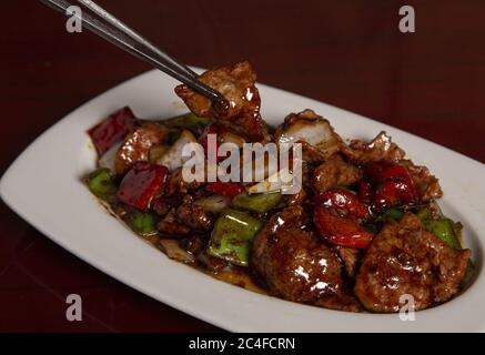 Colpo di closeup di chopsticks cinesi e un piatto di vitello con peperoni in salsa di fagioli Foto Stock