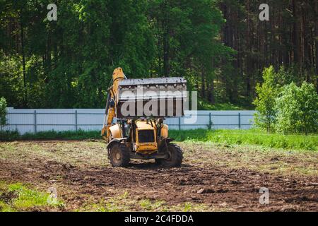 Compensazione e livellamento di un terreno privato. Escavatore giallo con benna grande e aperta Foto Stock