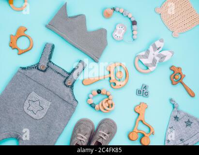 Concetto di accessori per bambini. Vestiti per bambini e giocattoli in legno su sfondo azzurro. Vista dall'alto, disposizione piatta. Foto Stock