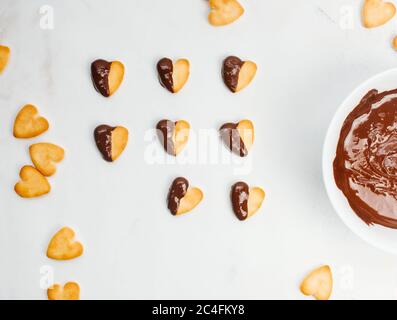 Biscotti a forma di cuore per San Valentino ricoperti di cioccolato su sfondo di marmo chiaro. Vista dall'alto, disposizione piatta. Foto Stock