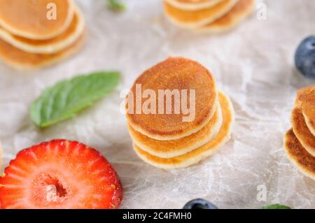 Dolci frittelle fatte in casa con fragole e mirtilli su carta pergamena bianca.sfondo alimentare. Disposizione piatta. Orizzontale. Foto Stock