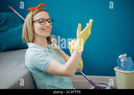 Donna felice che indossa guanti di gomma gialla prima della pulizia Foto Stock