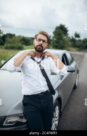 Uomo sicuro in camicia bianca appoggiato su un'auto moderna Foto Stock