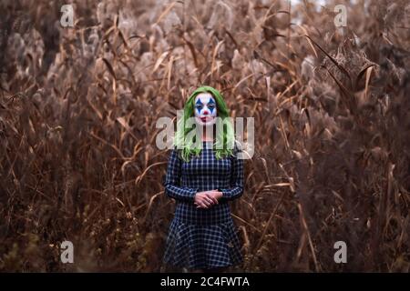 Ritratto di una ragazza con capelli verdi con trucco joker su un arancio foglie di sfondo canne. Foto Stock