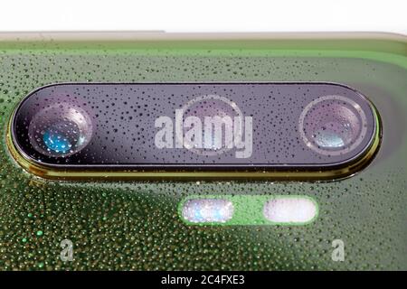 obiettivo verde della fotocamera del telefono coperto da piccole gocce d'acqua - primo piano con messa a fuoco e sfocatura selettive Foto Stock