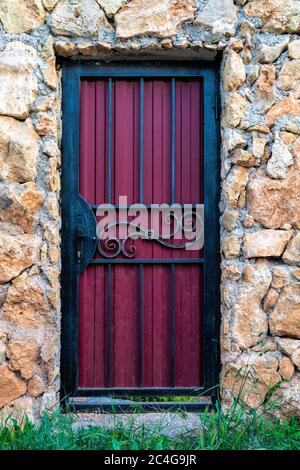 Una porta in metallo viola con una manopola nera. La porta è in un muro di roccia. Sfondo di muratura calcarea. Il muro è fatto di pietra selvatica. Il Foto Stock