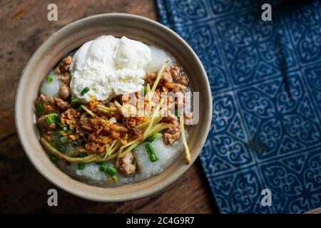 Colazione in stile thailandese con zuppa di riso di maiale e uova su tavolo di legno. Spazio per la copia mettere il testo sullo sfondo. Foto Stock